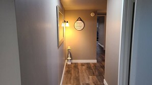 Un corridoio con pavimento in legno, un lampadario a parete e una citazione motivazionale incorniciata.