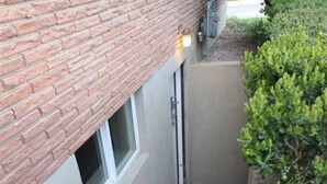Stretto corridoio esterno con parete in mattoni, una finestra e una porta.