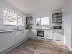A modern kitchen with white cabinets, a built-in oven, and a microwave. - Charming Hayling House with Garden - Pass the Keys (Hayling Island)
