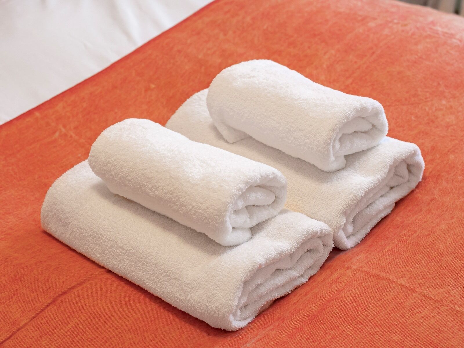 A neatly folded white towel on an orange bedspread.