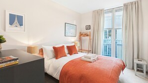 A hotel room with a bed, a bedside table, a lamp, a framed picture of the Eiffel Tower, a window with curtains, and a balcony. - Perfectly Located Comfy 1-Bed in London Bridge - Pass the Keys (London)