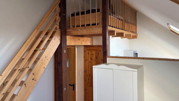 A wooden staircase leading to a loft bedroom with a slanted ceiling.
