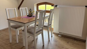 A dining area with a wooden table and white chairs, a window with a view, and a white radiator.