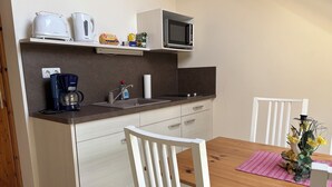 A compact kitchen with a microwave, kettle, coffee maker, and a small shelf with food items.