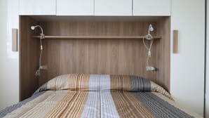 Ein ordentlich bezogenes Bett mit gestreifter Bettwäsche, ein hölzerner Kopfteil und zwei an der Wand befestigte Leuchten.