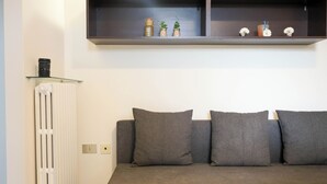 Ein Wohnzimmer mit grauem Sofa, weißem Heizkörper und einer Vitrine mit Dekorationen.