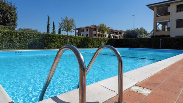 Ein Schwimmbecken mit Metallgeländern, umgeben von einer gefliesten Terrasse und einer Hecke.