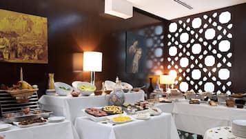 Montaje de bufé con diferentes alimentos y una pared decorativa con recortes geométricos.