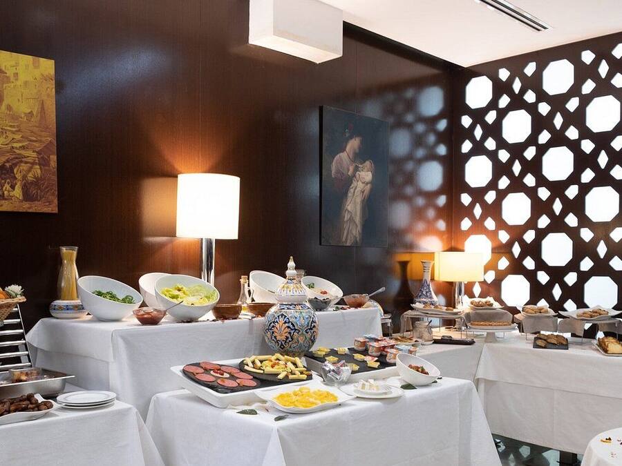 Montaje de bufé con diferentes alimentos y una pared decorativa con recortes geométricos.