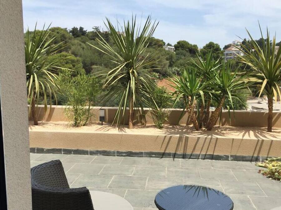 A patio with a round table and chairs, surrounded by palm trees and a view of a hillside with buildings.