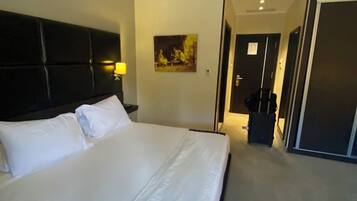 A hotel room with a large bed, a headboard, a painting on the wall, and a door leading to another room.