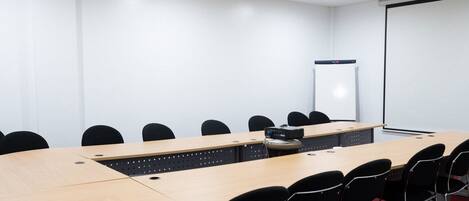 Een vergaderzaal met een lange tafel, zwarte stoelen, een projectorscherm en een whiteboard.