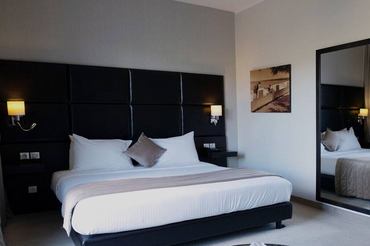 Een moderne hotelkamer met een groot bed, twee nachtkastjes, een hoofdbord en een spiegel.