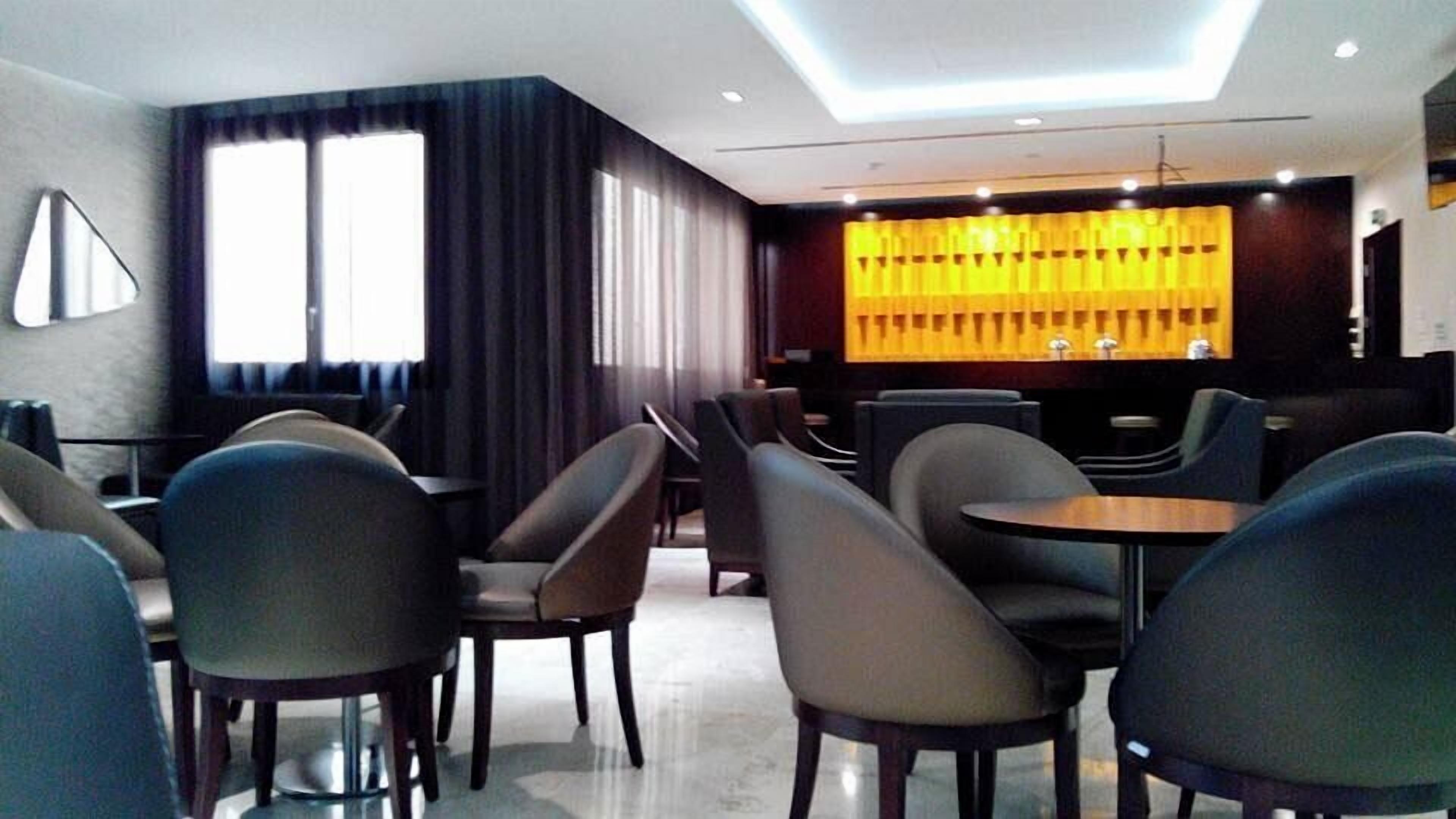Un moderno vestíbulo de hotel con zona de bar, arreglos de asientos y un gran ventanal con cortinas.