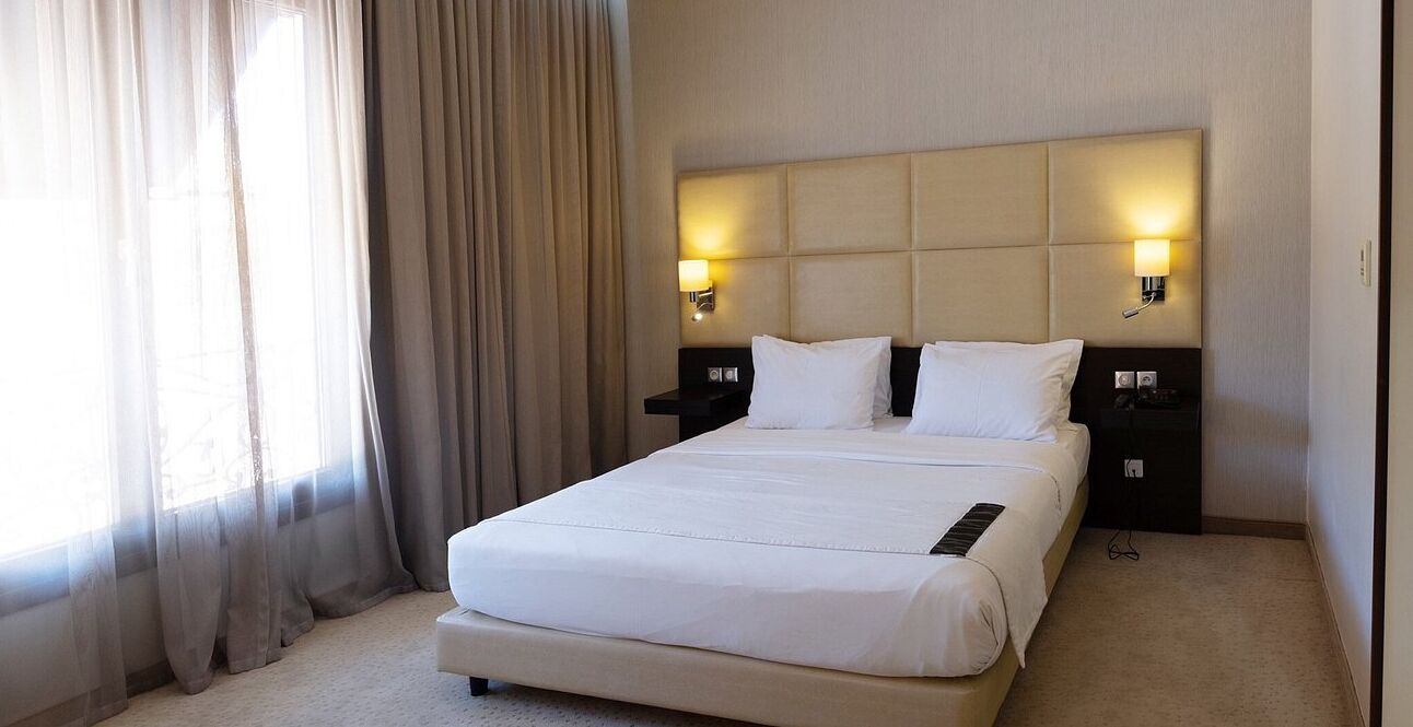 Een hotelkamer met een groot bed, twee nachtkastjes met lampen en een raam met gordijnen.