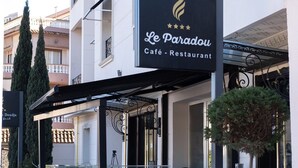 Un edificio con un cartello che riporta "Le Paradou Café - Restaurant" e un balcone con ringhiera.