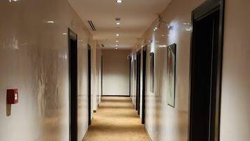 Un largo pasillo de hotel, estrecho, con alfombra estampada, luces empotradas y puertas a ambos lados.