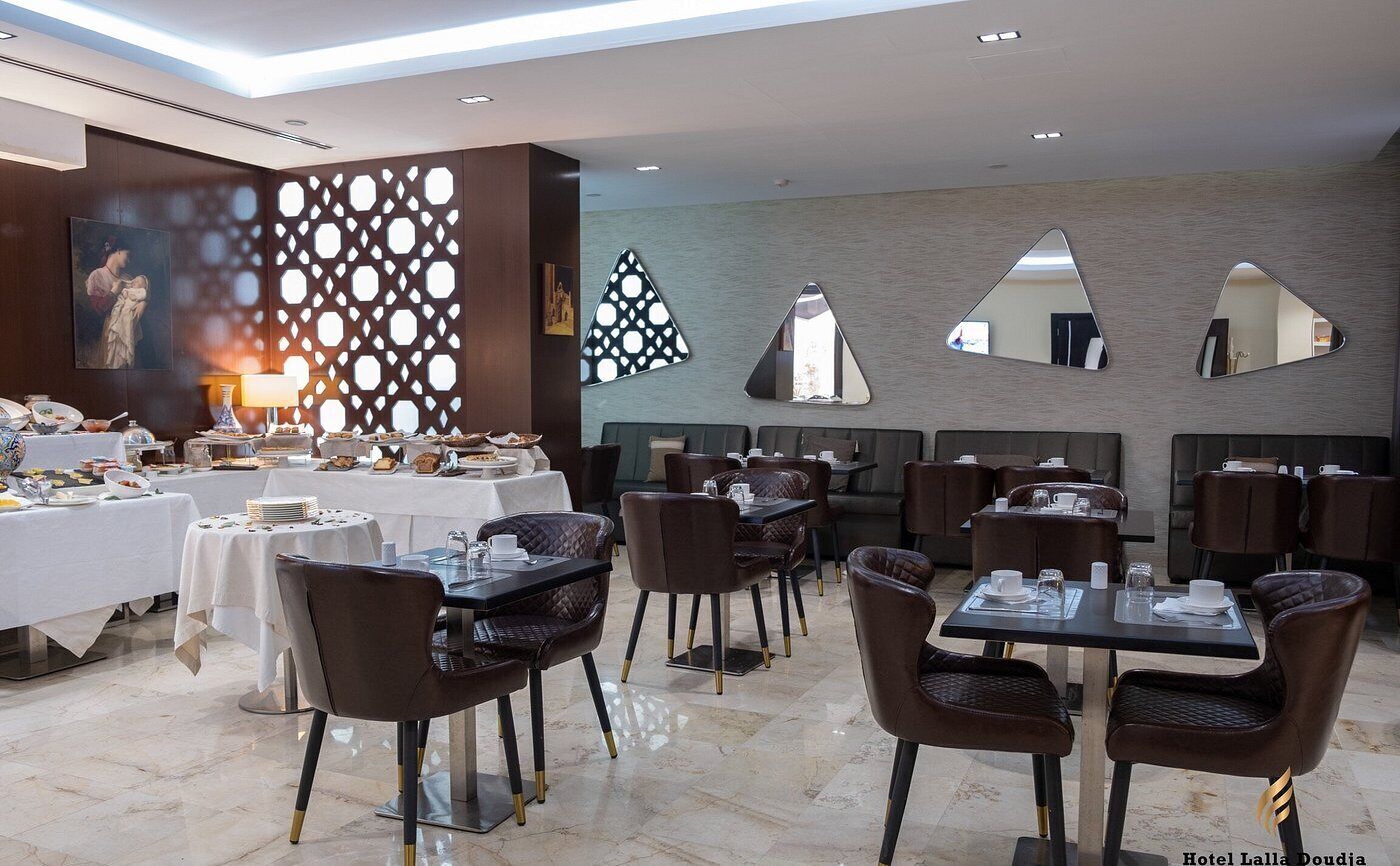 Un comedor moderno con mesas y sillas, una pared decorativa con patrones geométricos y un cuadro grande.