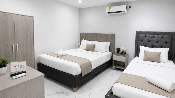A modern hotel room with two beds, a wardrobe, a bedside table with a phone, and a welcome sign. - ULTIMO DEL SEMANA (San Andrés)