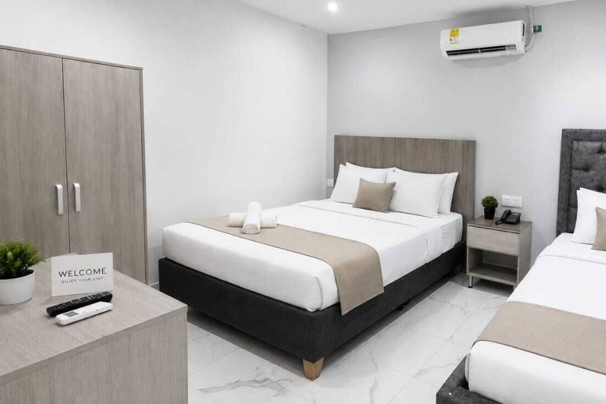 Una habitación de hotel moderna con dos camas, un armario, una mesita de noche con teléfono y un cartel de bienvenida.