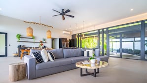 A modern living room with a grey sofa, a round coffee table, and a ceiling fan. - Modern 5BR Villa • Sunset Views • Near Dominical (Hatillo de Aguirre)