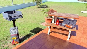 A barbecue setup with a grill, a portable gas canister, and a toolbox on a wooden bench.