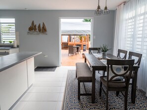 A modern kitchen with a dining area, featuring a large window, a patterned rug, and a view of the outdoor patio.