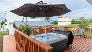 Un jacuzzi en una terraza de madera, con una sombrilla grande que da sombra.