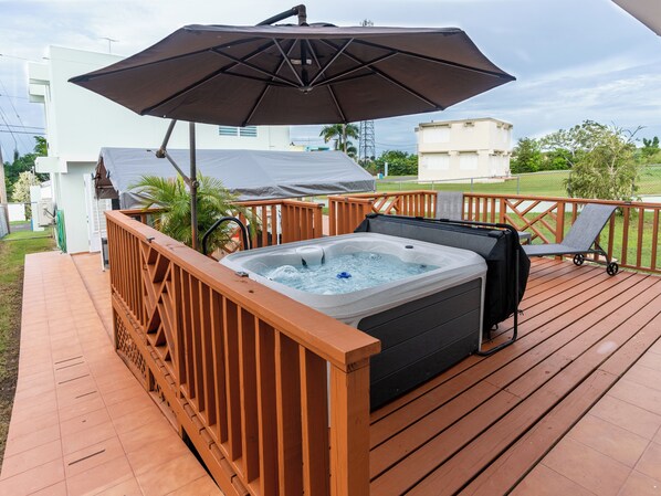 A hot tub on a wooden deck with a large umbrella providing shade.