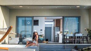 A modern outdoor living area with a pool, seating, and a dining setup. - Zoe Luxury Seafront Villa with Heatable Pool, Villa (Heraklion)