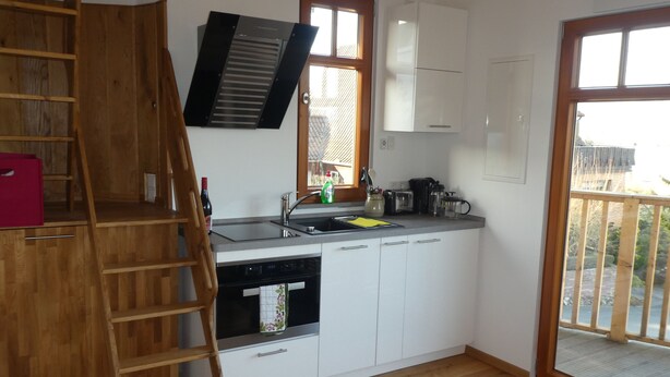 Une cuisine avec des meubles blancs, une échelle en bois, un évier et une fenêtre donnant sur une terrasse.