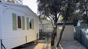 A mobile home with a fenced yard, a tree, and another building in the background. - MOBILE-HOME 1 BEDROOM WITH AIR-CONDITIONING SOUTH ARDÈCHE (07) ORGNAC-L'AVEN (Orgnac-l'Aven)