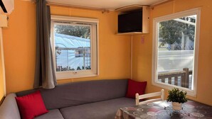 A cozy room with a sofa, a table with a plant, and two windows with curtains. - MOBILE-HOME 1 BEDROOM WITH AIR-CONDITIONING SOUTH ARDÈCHE (07) ORGNAC-L'AVEN (Orgnac-l'Aven)