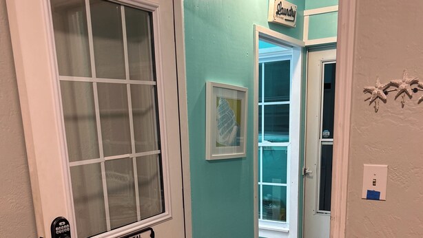 Entree van een strandbungalow met een glazen deur, een bord waarop 'Wasserij' staat en een ingelijst kunstwerk aan de muur.