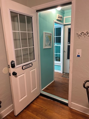 A coastal bungalow entrance with a glass door, a sign reading "Laundry," and a framed artwork on the wall.