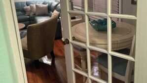 Een kamer met een eettafel, stoelen, een bank en een deur met een ruit.
