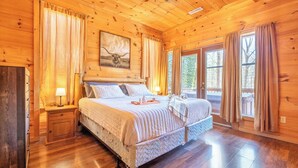 A wooden cabin bedroom with a large bed, two bedside tables, a nightstand, and a window with curtains. - *Spacious 4BD Lodge w/ POOL! Hot Tub + GAMES!* (Sevierville)