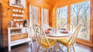 A wooden cabin interior with a dining table set for four, surrounded by chairs with yellow cushions. - *Spacious 4BD Lodge w/ POOL! Hot Tub + GAMES!* (Sevierville)
