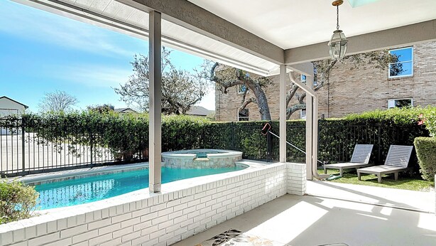 A modern outdoor pool area with a hot tub, lounge chairs, and a view of the neighborhood.