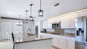 A modern kitchen with white cabinetry, granite countertops, stainless steel appliances, and pendant lighting.