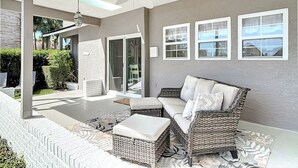 A covered patio area with wicker furniture, a ceiling fan, and a view of the outside.