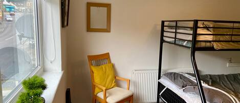 Een kamer met een stapelbed, een stoel, een radiator en een raam met uitzicht op de straat.