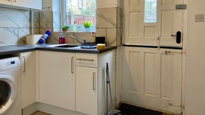 A compact kitchen with a washing machine, a sink with a window above it, and a door with a handle. - Cosy Contractors Retreat in Batley - Sleeps 3 (Batley)