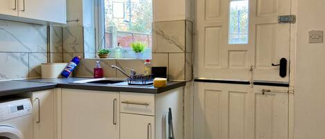 A compact kitchen with a washing machine, a sink with a window above it, and a door with a handle.