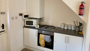 A compact kitchen with a microwave, gas stove, oven, and a fire extinguisher on the wall. - Cosy Contractors Retreat in Batley - Sleeps 3 (Batley)
