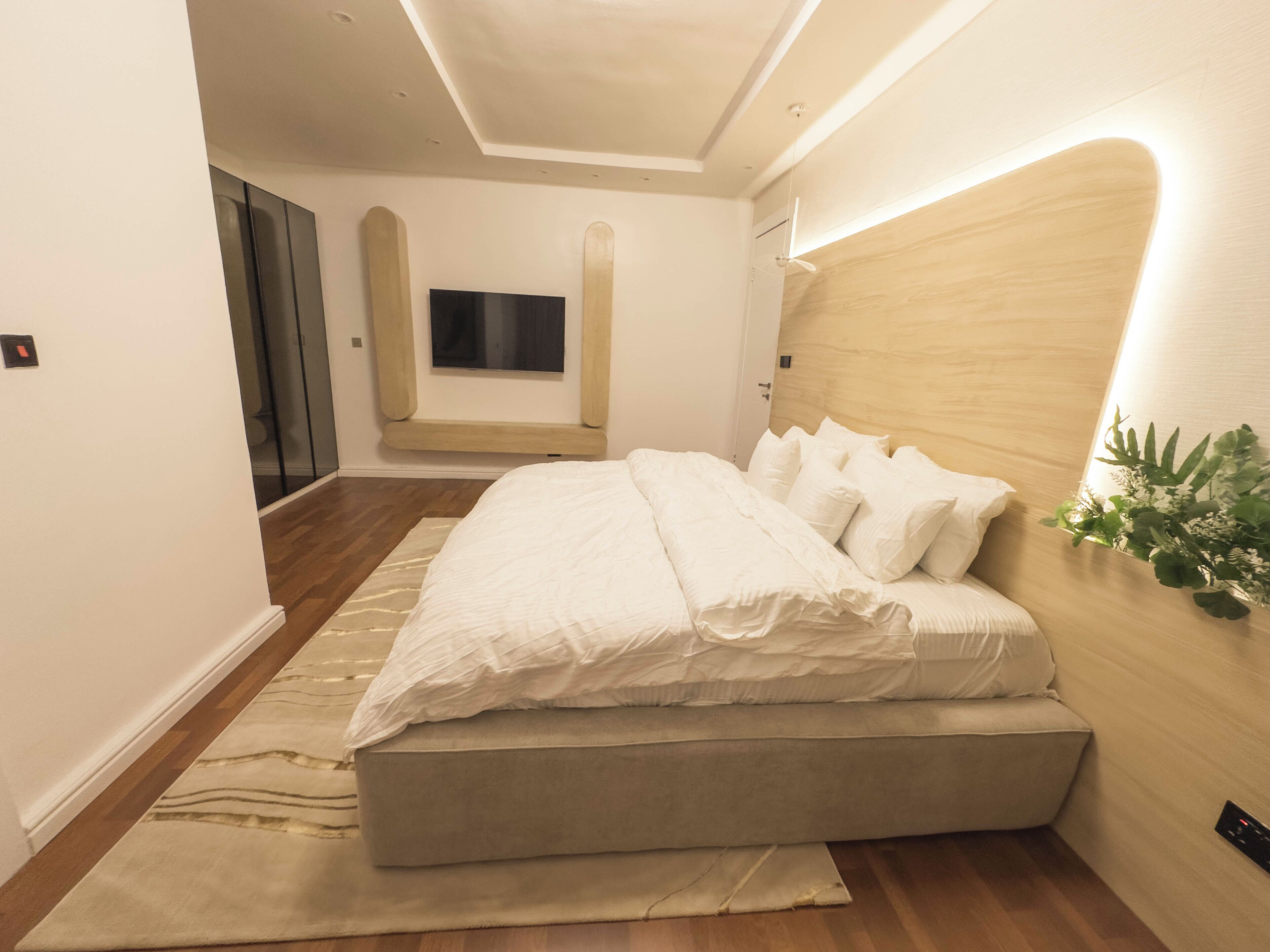Une chambre à coucher moderne avec un grand lit, un téléviseur à écran plat et une tête de lit en bois.