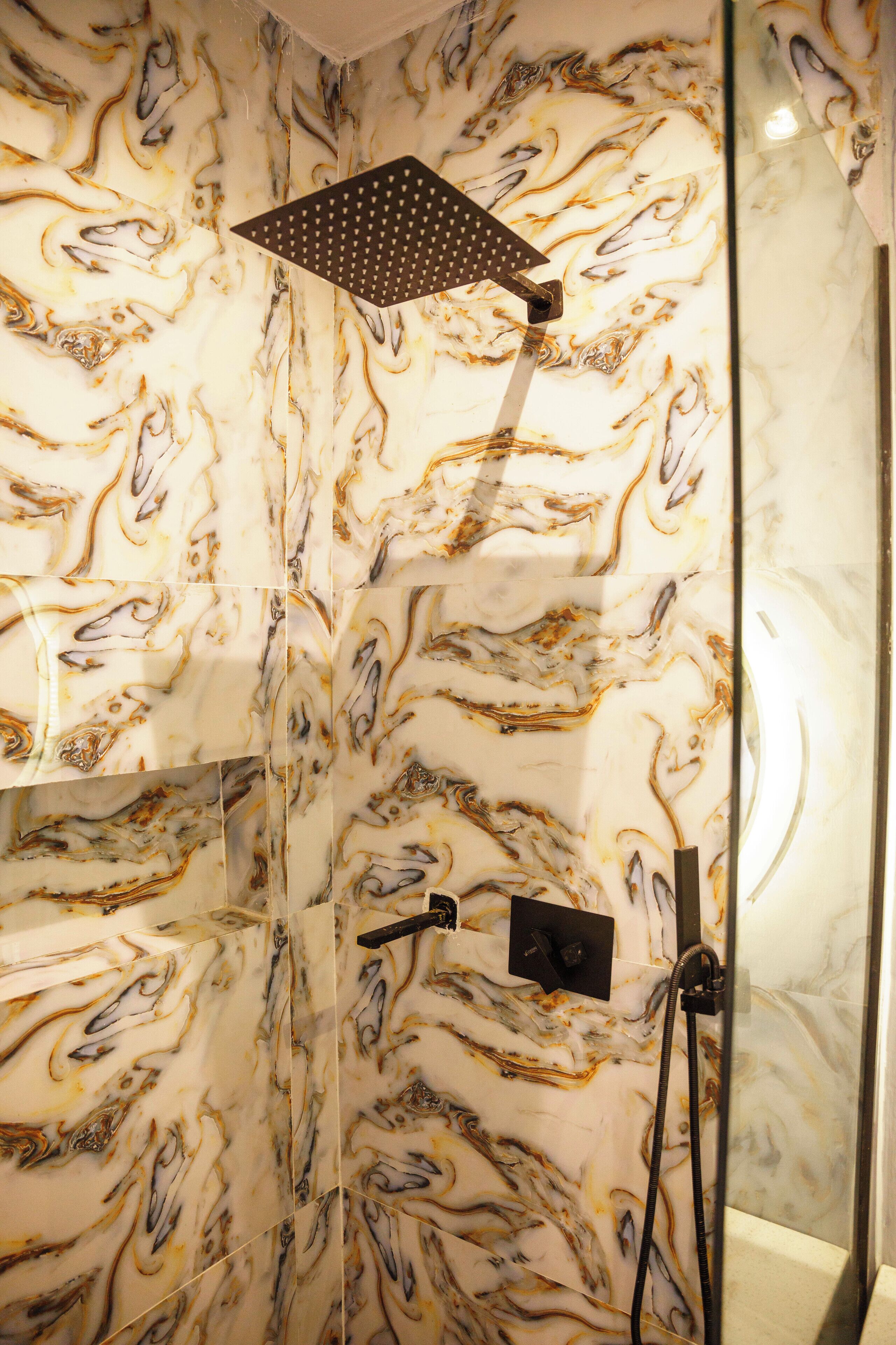 Une douche avec un mur aux motifs de marbre et une pomme de douche moderne.