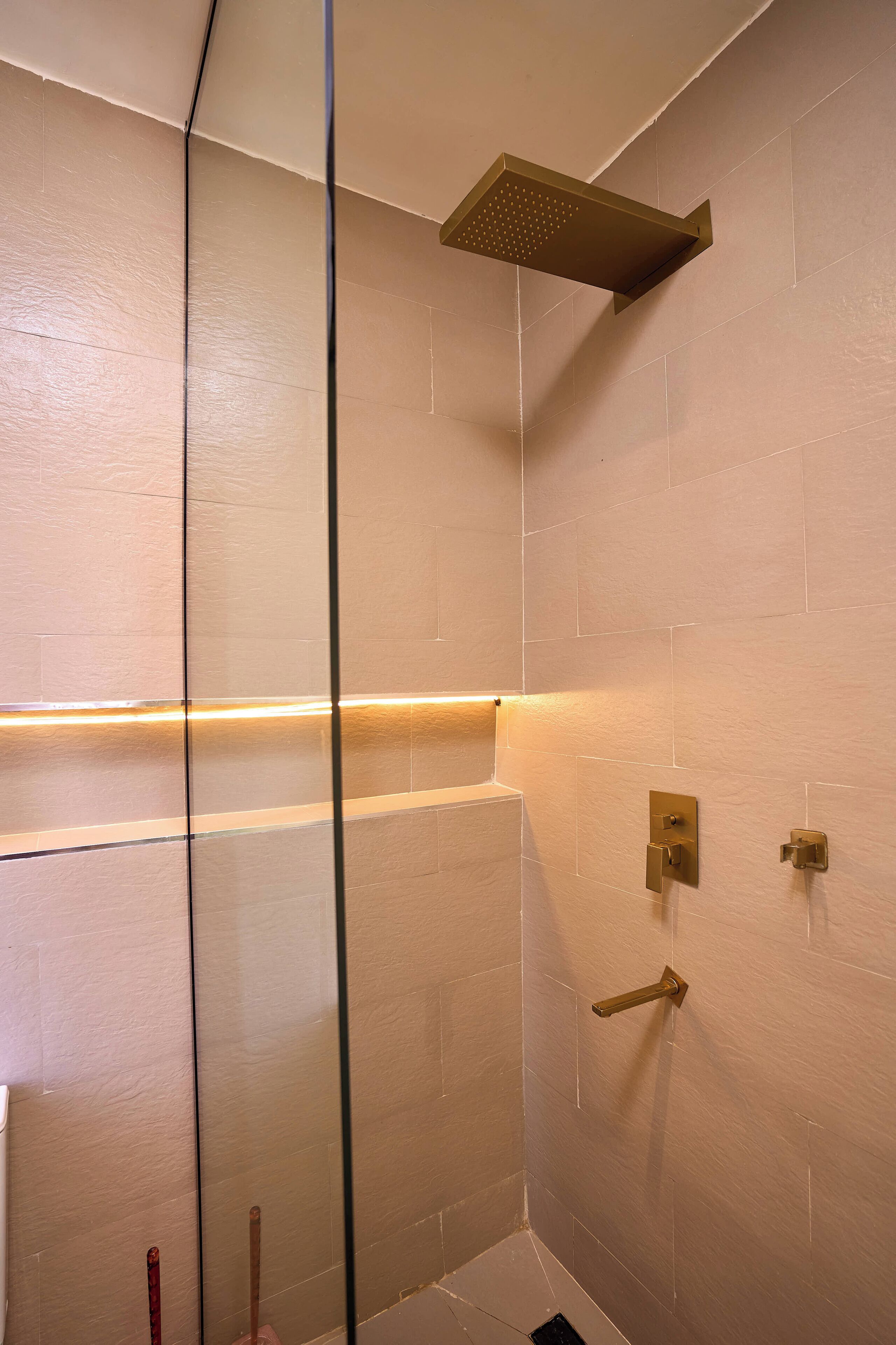 A shower with a squarehead showerhead, a glass partition, and a wall-mounted control panel.