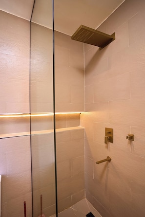 A shower with a squarehead showerhead, a glass partition, and a wall-mounted control panel. - Libertini Apartments by Ken-Legend (Lekki)