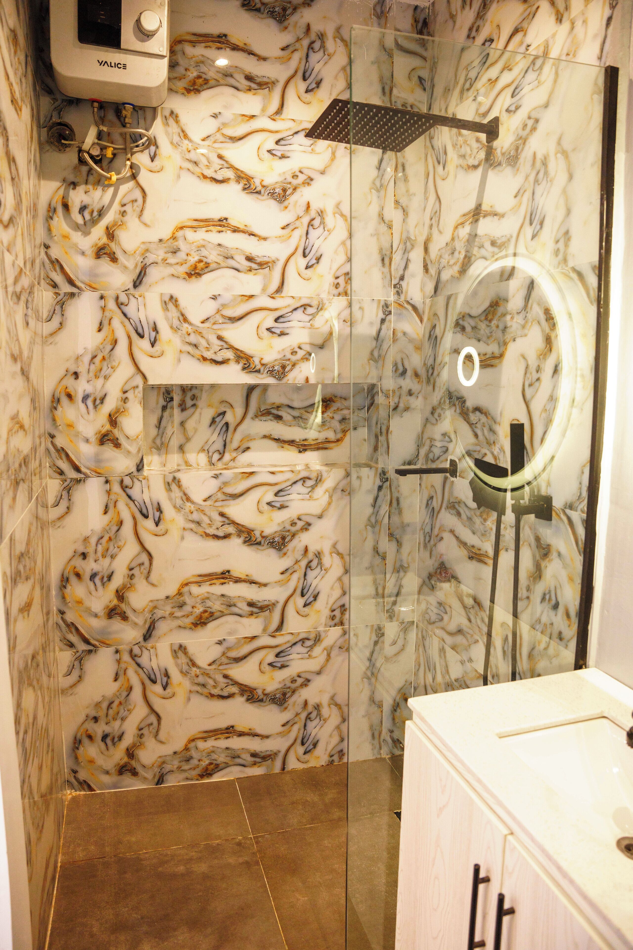 A bathroom with a marble wall, a glass shower enclosure, and a sink with a mirror.
